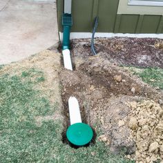 a green and white pipe sticking out of the ground in front of a house with grass