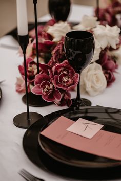 the table is set with black plates and pink napkins, candles, and flowers