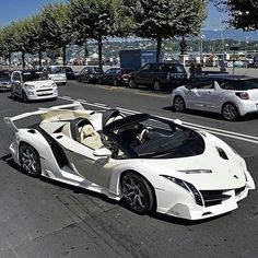 a white sports car is driving down the street with other cars in the back ground