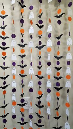 a group of halloween decorations with bats and ghost faces hanging from strings on a wall