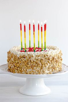 a birthday cake with seven lit candles on it and peanuts in the middle, sitting on a white pedestal