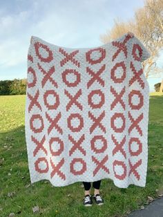 a woman standing in the grass holding up a red and white crocheted blanket