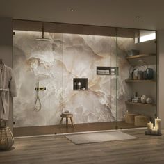 a bathroom with a glass shower door and shelves on the wall, along with a white rug