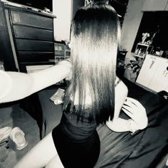 a woman with long hair sitting on a bed next to a dresser in a room