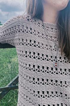 a close up of a person wearing a crocheted sweater in the grass near a fence