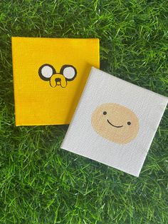 two pieces of paper with cartoon faces on them sitting in the grass next to each other