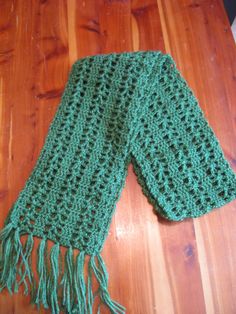 a green crocheted scarf sitting on top of a wooden floor