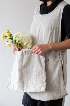 a woman is holding flowers in her hand while wearing a white linen apron and black shirt