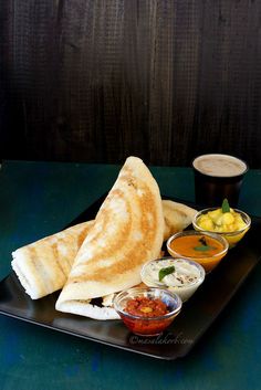 a black plate topped with food next to cups of sauces and condiments