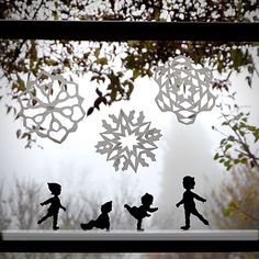 some paper cut snowflakes hanging from a window sill with trees in the background