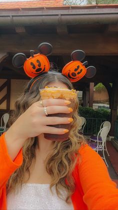 a woman wearing mickey ears and holding a sandwich in front of her face with pumpkins on it