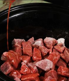 the meat is being cooked in the crockpot with sauce on top and red string