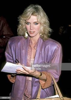 an older woman is holding a paper and looking at the camera while standing in front of other people