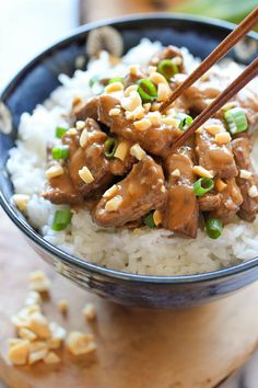 a bowl filled with rice and meat on top of a wooden cutting board next to chopsticks