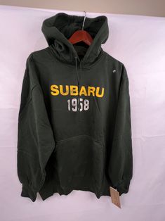 a green sweatshirt with the word subaru printed on it, hanging from a hanger