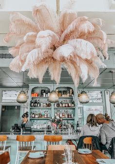 two people sitting at a table in a restaurant with large pink feathers hanging from the ceiling