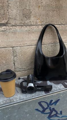 a black purse sitting next to a coffee cup on top of a cement slab with graffiti