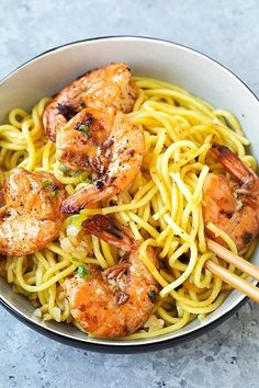 a bowl filled with noodles and shrimp on top of a table next to chopsticks