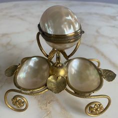 an ornate gold and white vase on a marble table top with leaves around the base