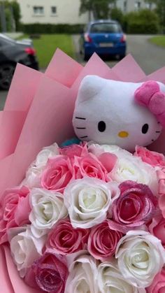 a hello kitty stuffed animal sitting in a bouquet of pink and white roses on the street