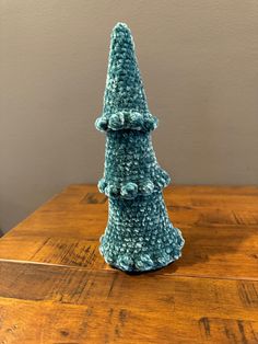 a crocheted blue christmas tree sitting on top of a wooden table next to a wall