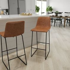 two brown chairs sitting next to each other on top of a hard wood floor in a kitchen