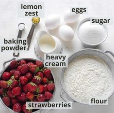 ingredients to make strawberry shortcakes laid out on a white counter top, including eggs, flour, sugar and strawberries