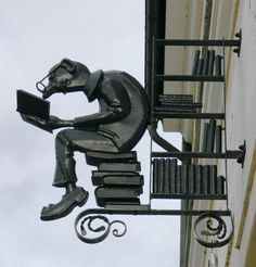 a statue of a man sitting on top of a book shelf next to a building