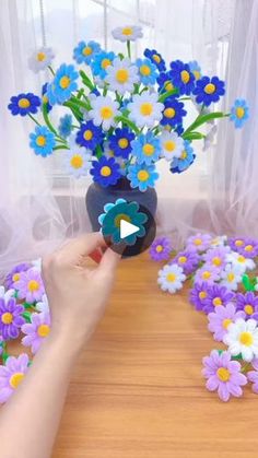 a person holding a fake flower in front of a vase filled with daisies and other flowers