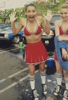 two women in red and white cheerleader outfits standing on skateboards with their hands up