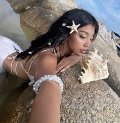 a beautiful woman laying on top of a rock next to the ocean holding a starfish