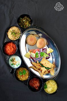 a silver plate topped with lots of different types of food next to bowls filled with sauces