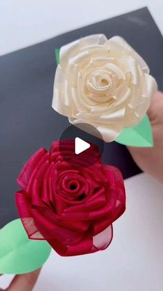 someone is holding two paper flowers in their hands, one red and the other white