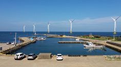 several cars are parked in the parking lot next to some windmills on the water