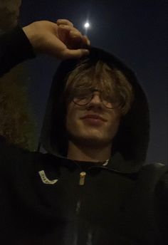 a young man wearing glasses and a hoodie is holding his hand up to the camera