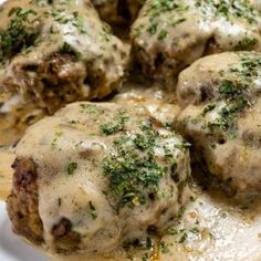 meatballs covered in gravy on a white plate with sauce and parsley