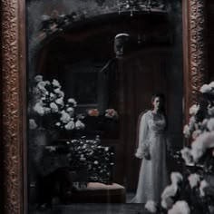 an old photo of a woman standing in front of a mirror with flowers on it