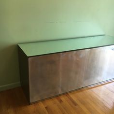 a shiny metal cabinet sitting on top of a hard wood floor next to a green wall