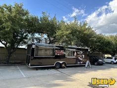 a food truck parked in a parking lot next to some trees and cars on the street