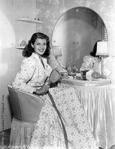 an old photo of a woman sitting at a table in front of a vanity mirror