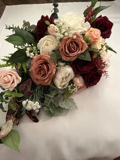 a bouquet of flowers sitting on top of a white tablecloth covered table with green leaves