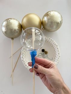 a hand holding a toothpick on top of a paper plate with gold balloons in the background