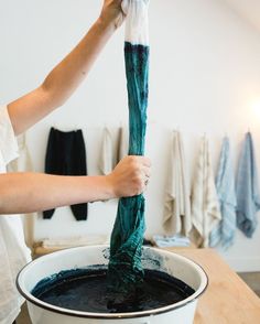 a person is washing their hands in a bucket filled with blue liquid and green hair