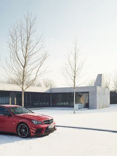 a red car parked in front of a building on a snow covered field with trees