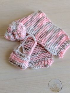 two pink and white knitted mittens sitting on top of a wooden table