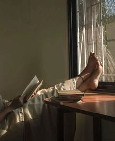 a person laying down reading a book in front of a window with their feet up