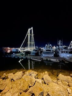 several boats are docked in the water at night time, with rocks on the shore