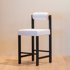 a black and white bar stool with a padded seat on a wooden floor in front of a beige wall