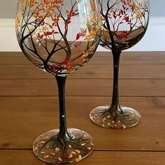 two wine glasses sitting on top of a wooden table next to each other with leaves painted on them