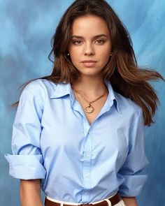 a woman in a blue shirt and white pants posing for a photo with her hands on her hips